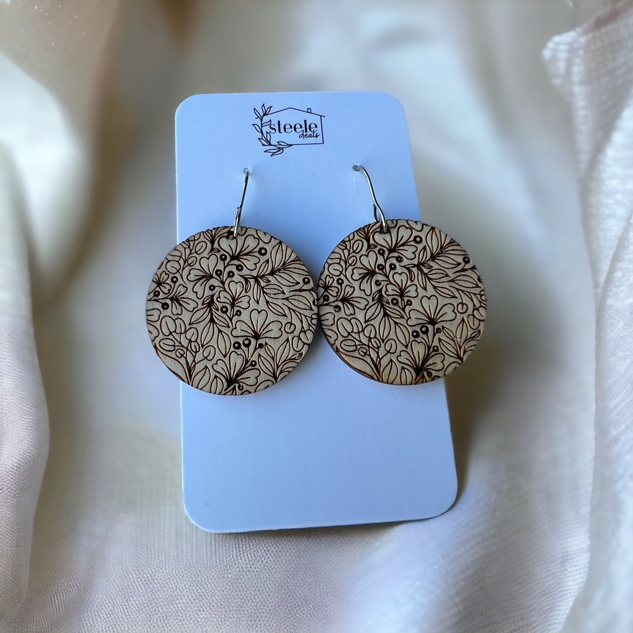 wood dangle earrings in the shape of a circle with an engraved floral pattern design