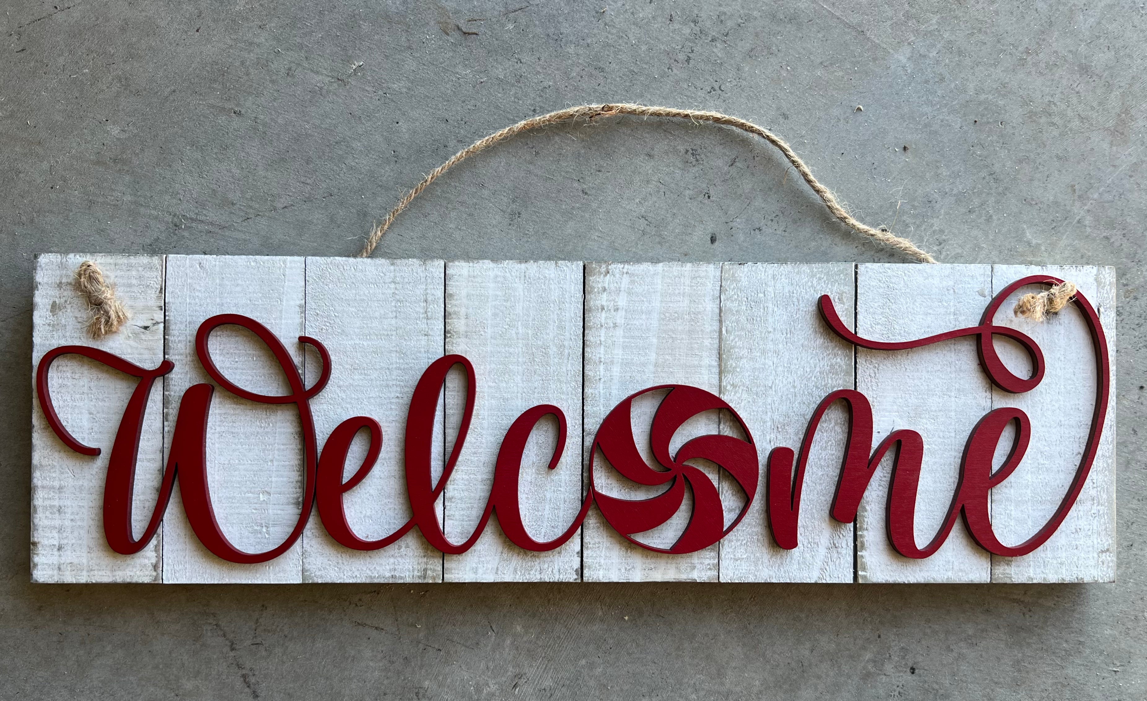 white wooden sign with WELCOME in red and the shape of a peppermint as the O
