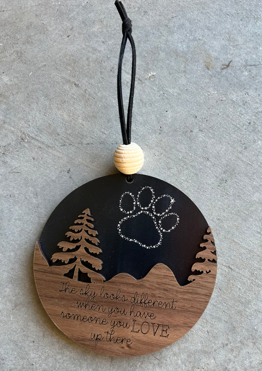 Phrase: The sky looks different when you have someone you love up there. Paw prints black background. wooden ornament.