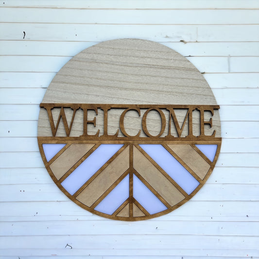 wooden circle sign with WELCOME in the center and angled stripped design on the bottom
