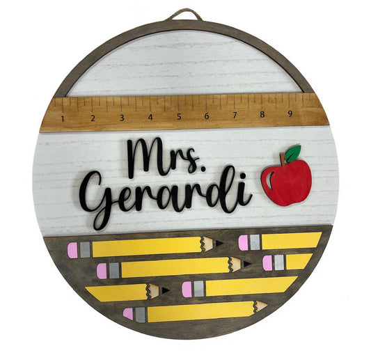 Personalized teacher sign with a ruler at the top, name and red apple in the center, and bottom filled with yellow pencil designs