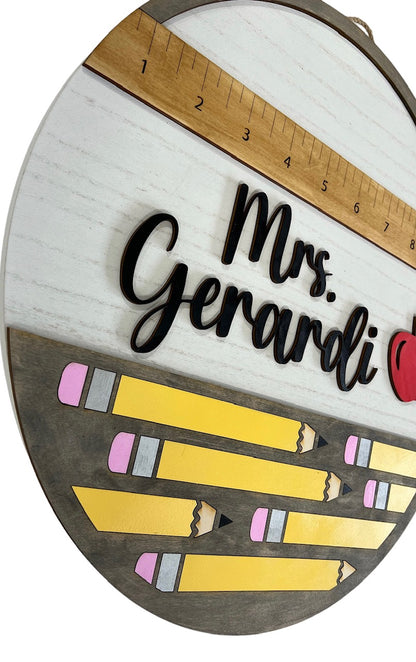 Personalized teacher sign with a ruler at the top, name and red apple in the center, and bottom filled with yellow pencil designs