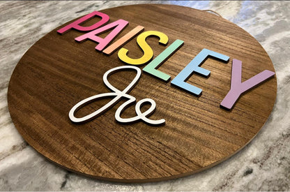 circle wooden sign with rainbow design for the first name and solid white for middle name