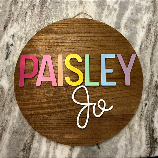 circle wooden sign with rainbow design for the first name and solid white for middle name